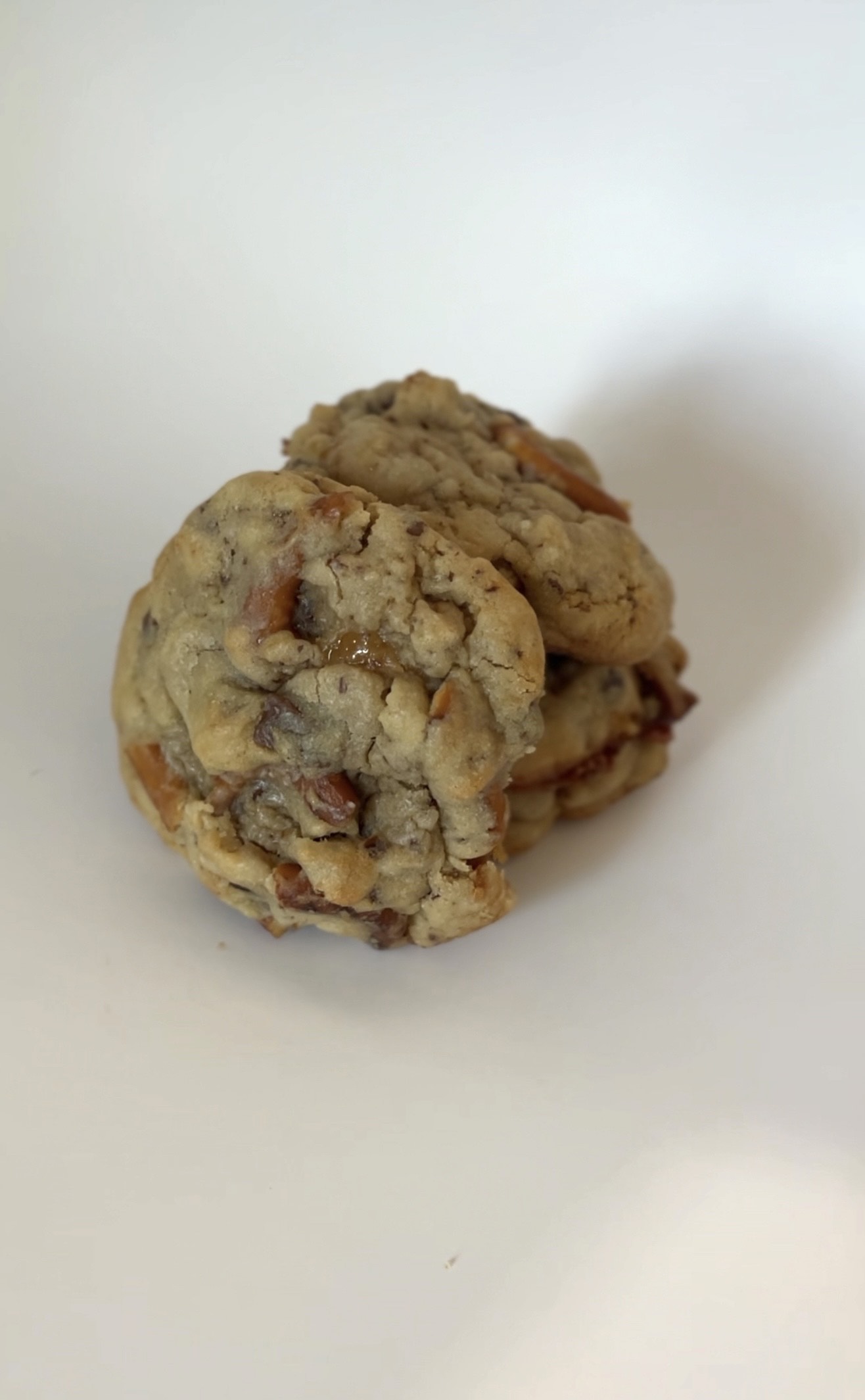Side view chewy salted caramel pretzel cookie with golden brown edges, with gooey caramel bits and topped with crunchy pretzel twists and flaky sea salt