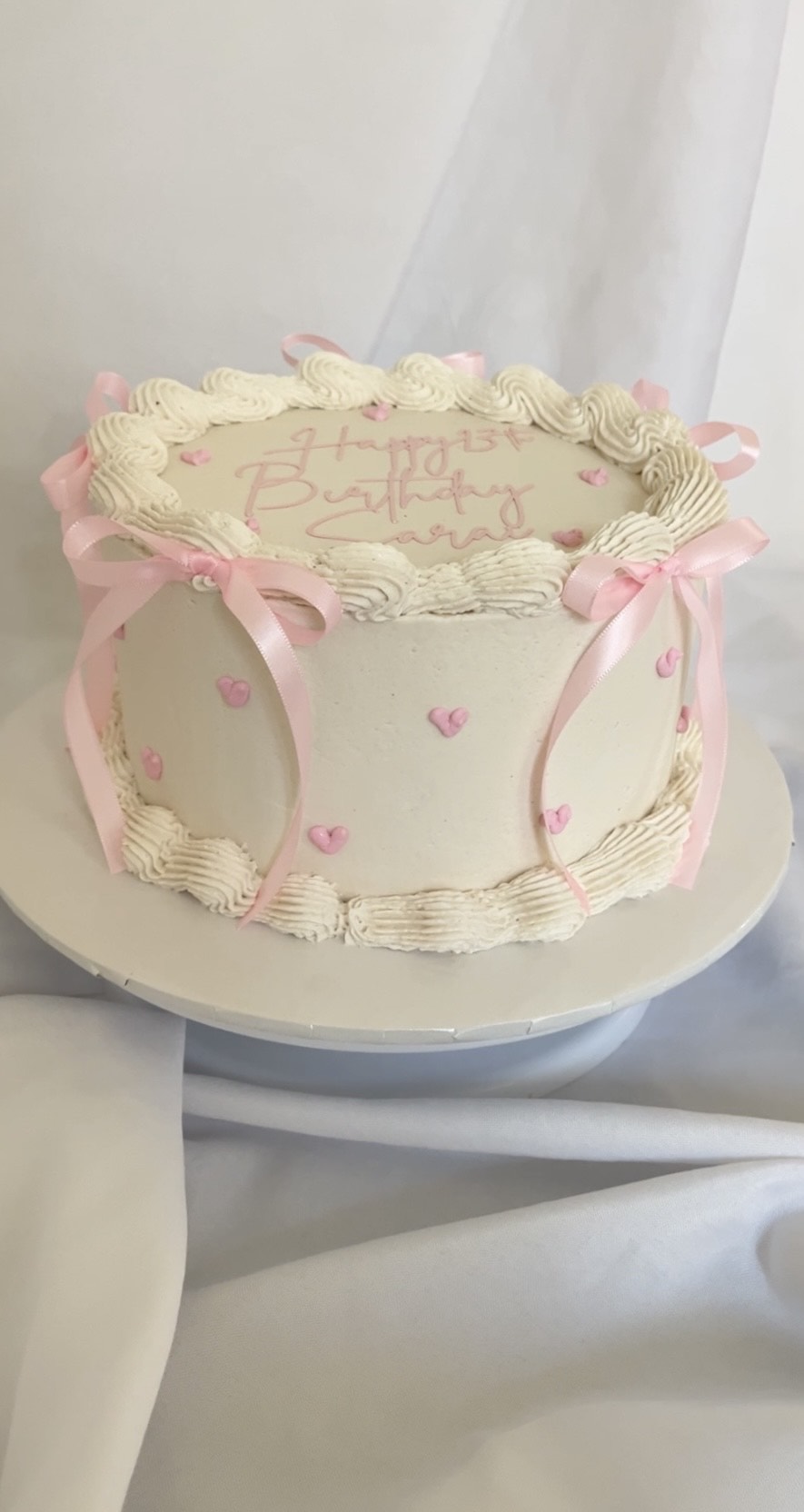 side view of vintage style coquette buttercream cake showing ribbon bows and hearts with “Happy Birthday Sarai”